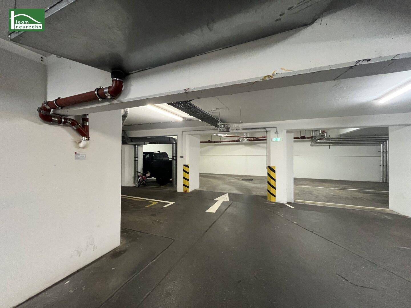 Geräumige Tiefgarage mit markierten Stellplätzen und sichtbaren Rohren an der Decke.