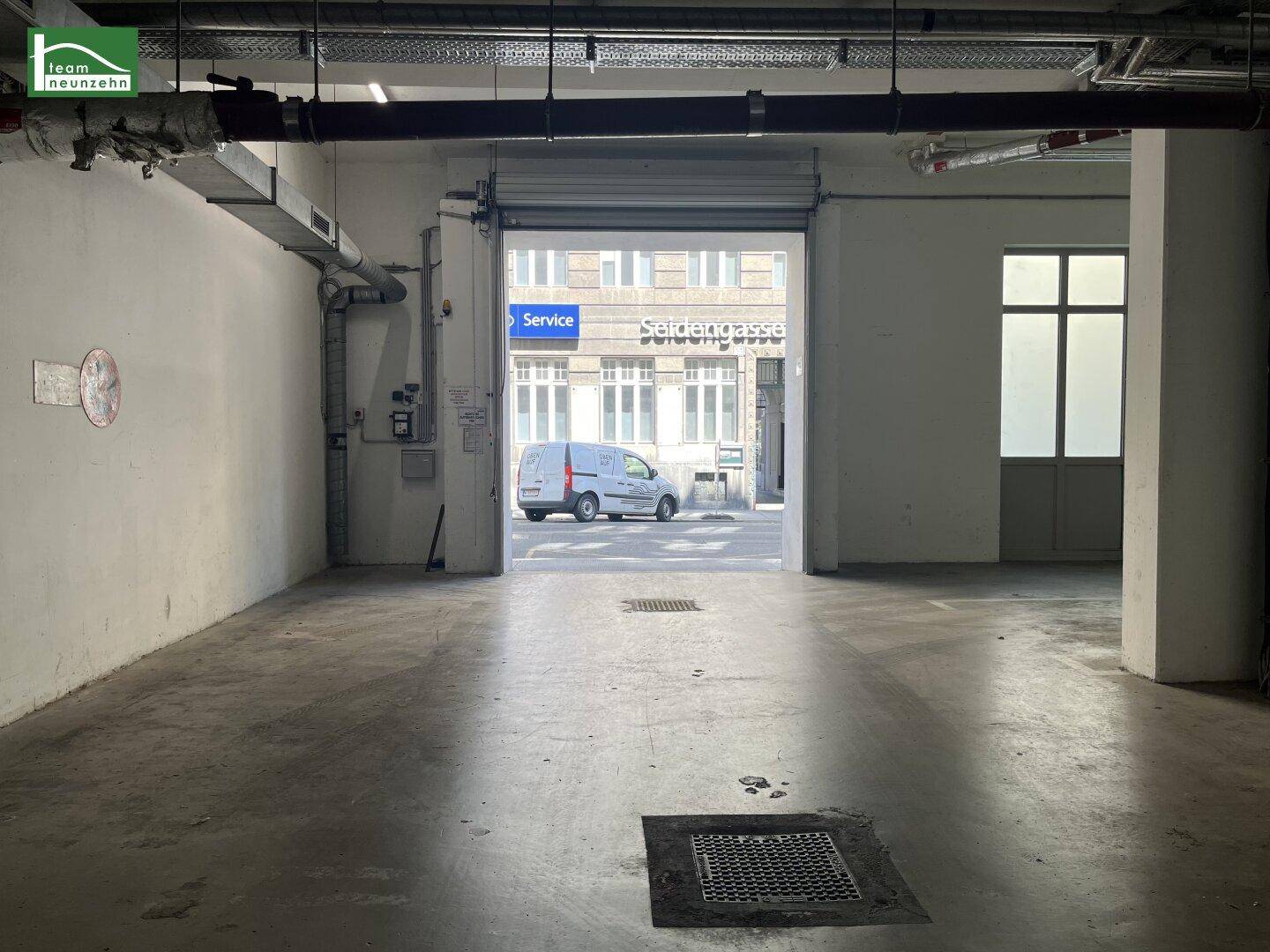 Leerer Garagenraum mit Rolltor, das den Blick auf die Straße und ein geparktes Fahrzeug freigibt.