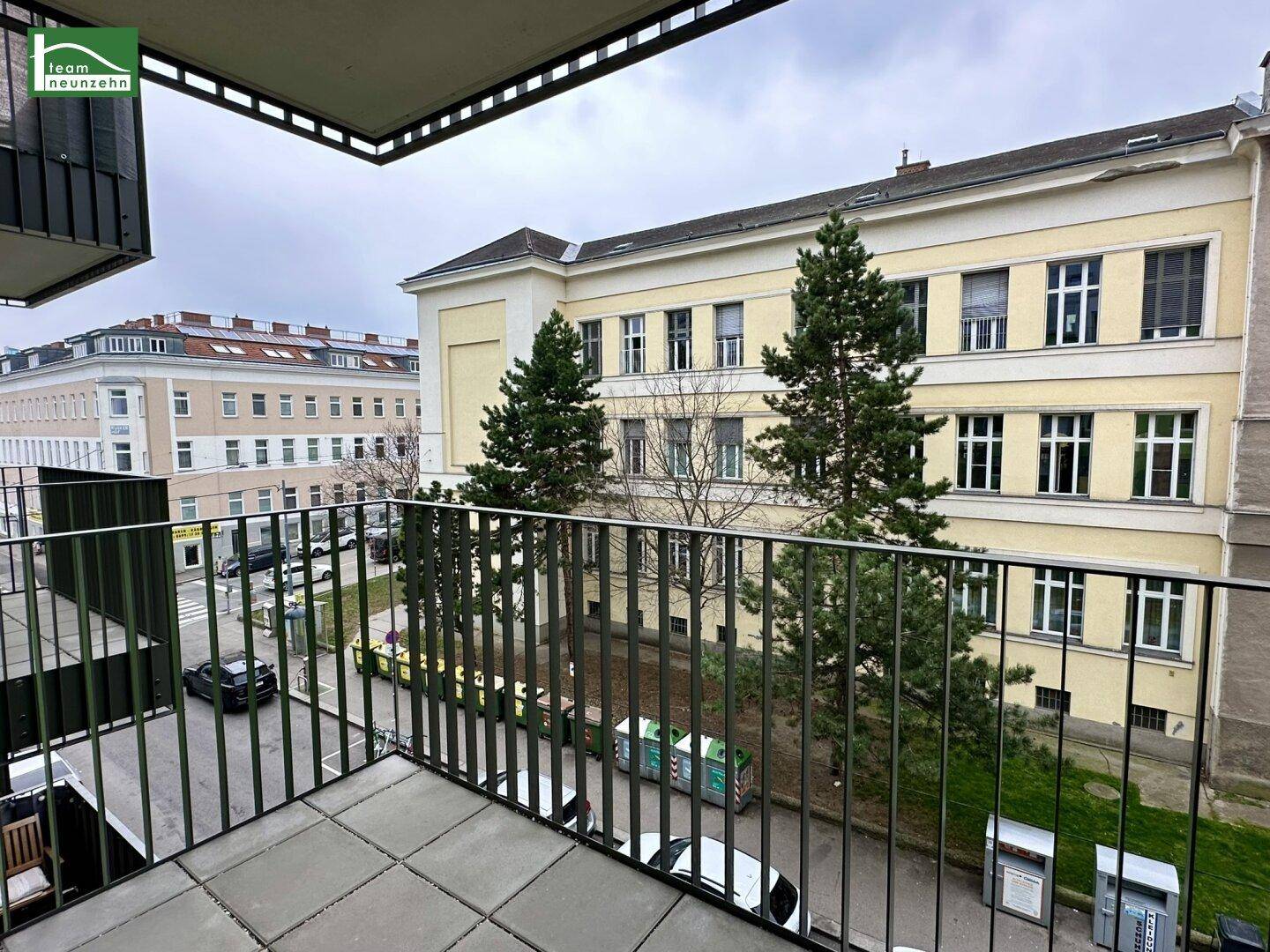Blick vom Balkon auf die Straße, Bäume und ein gegenüberliegendes Gebäude.