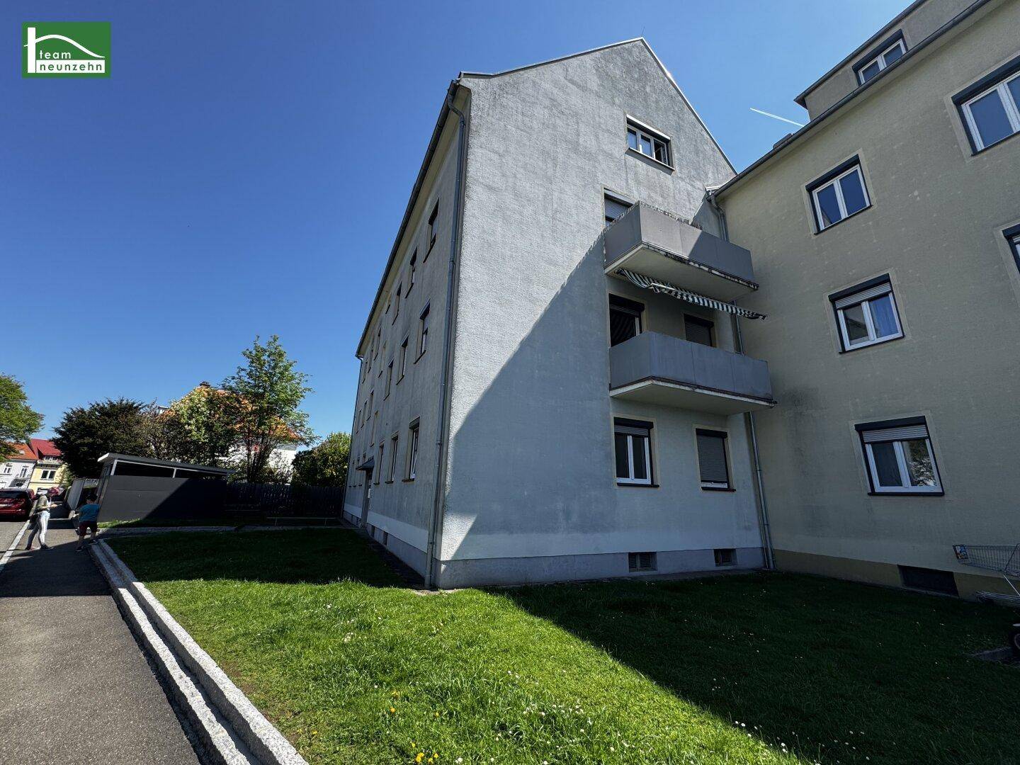 Wohngebäude mit heller Fassade, einem gepflegten Rasenstreifen und einem Gehweg daneben.