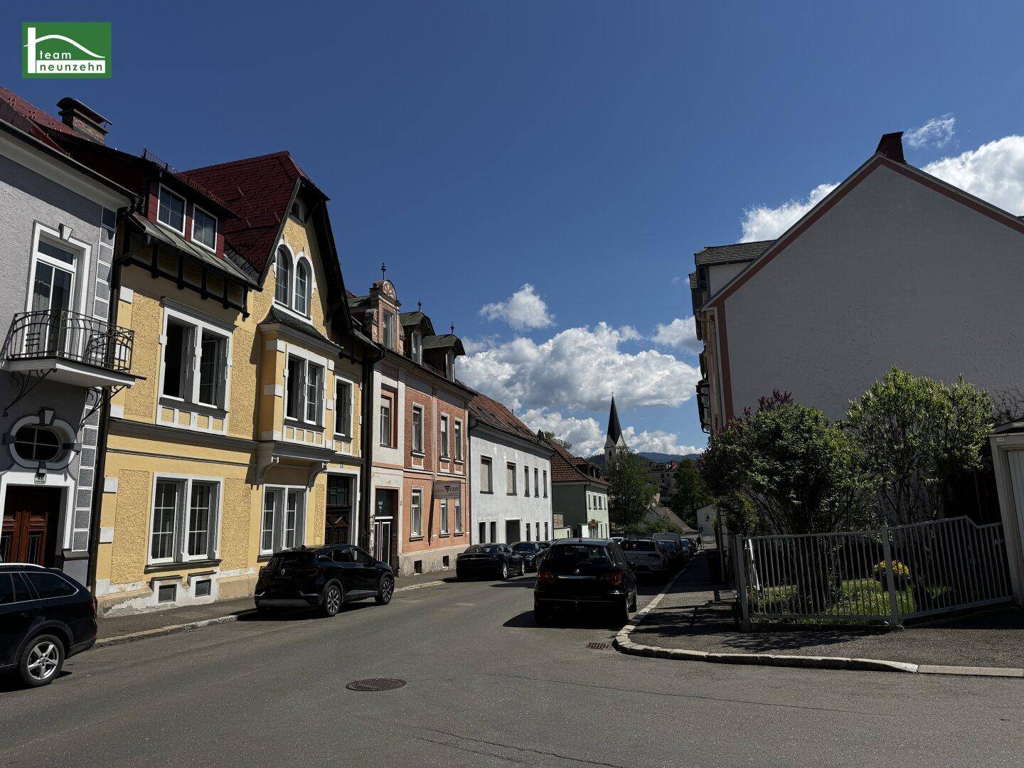 Malerische Straße mit traditionellen Gebäuden und geparkten Autos unter einem klaren blauen Himmel.