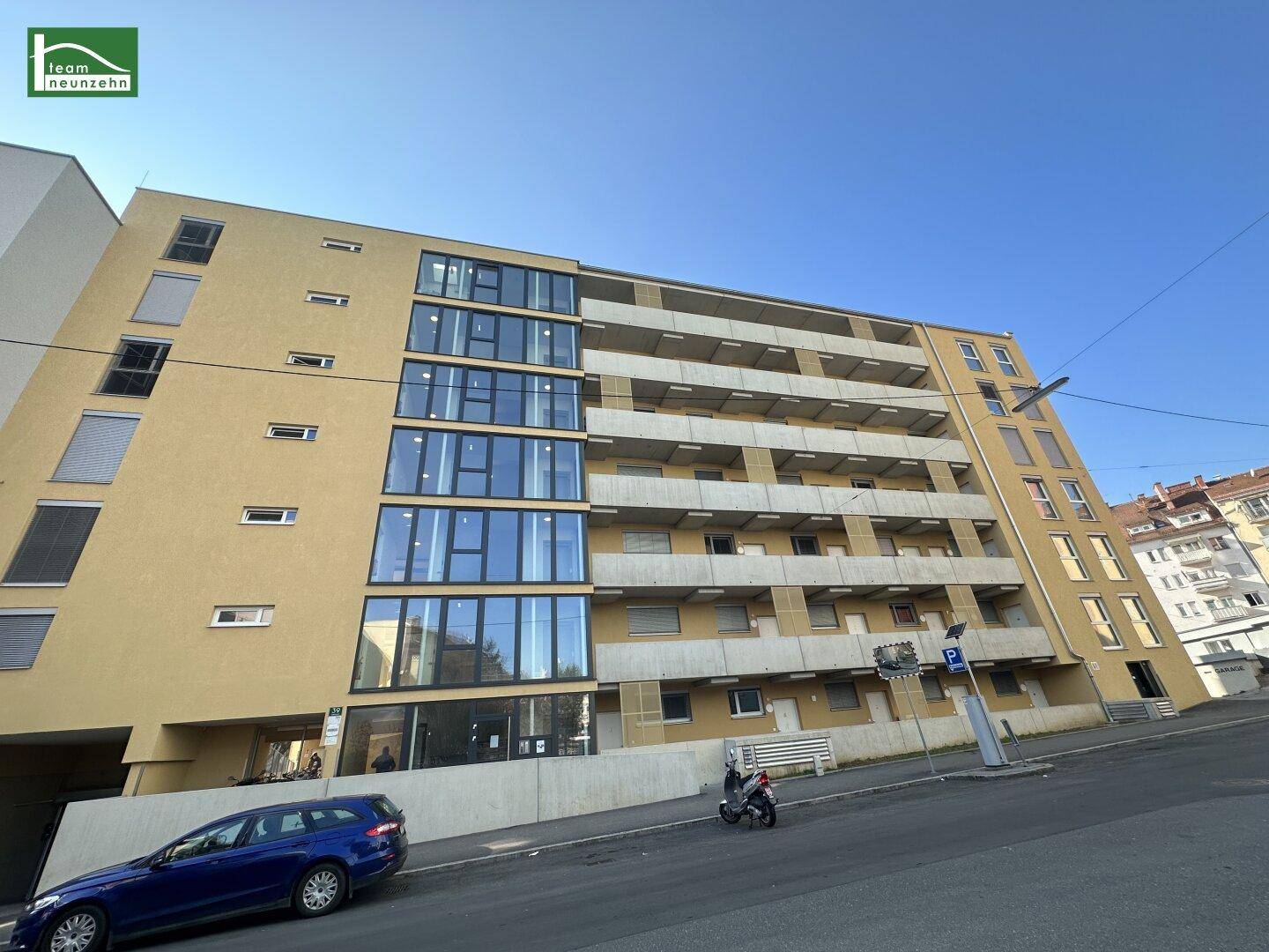 Mehrstöckiges Apartmentgebäude mit gelber Fassade, vielen Fenstern und Balkonen von der Straße aus gesehen.