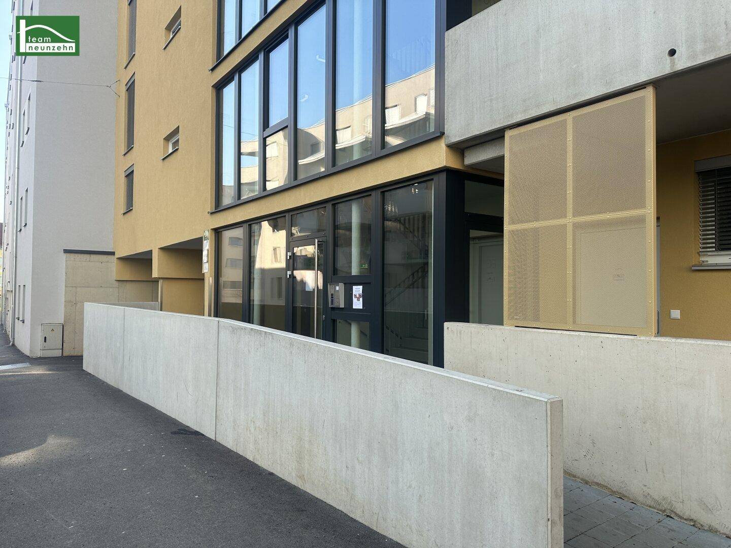 Eingangsbereich eines modernen Apartmentgebäudes mit einer barrierefreien Rampe und großen Glasfenstern.