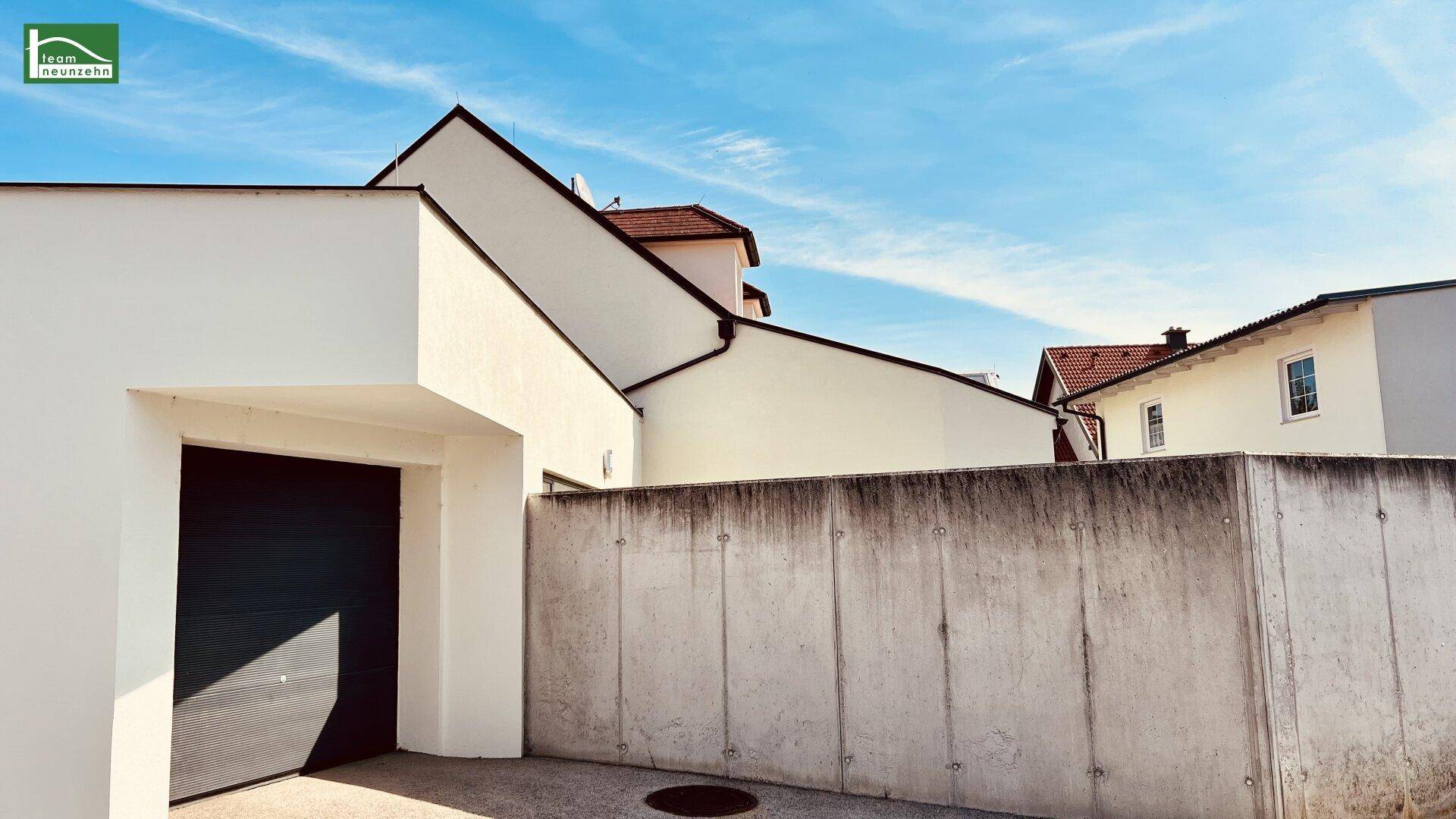 Außenansicht mit Betonmauer und Garageneinfahrt.
