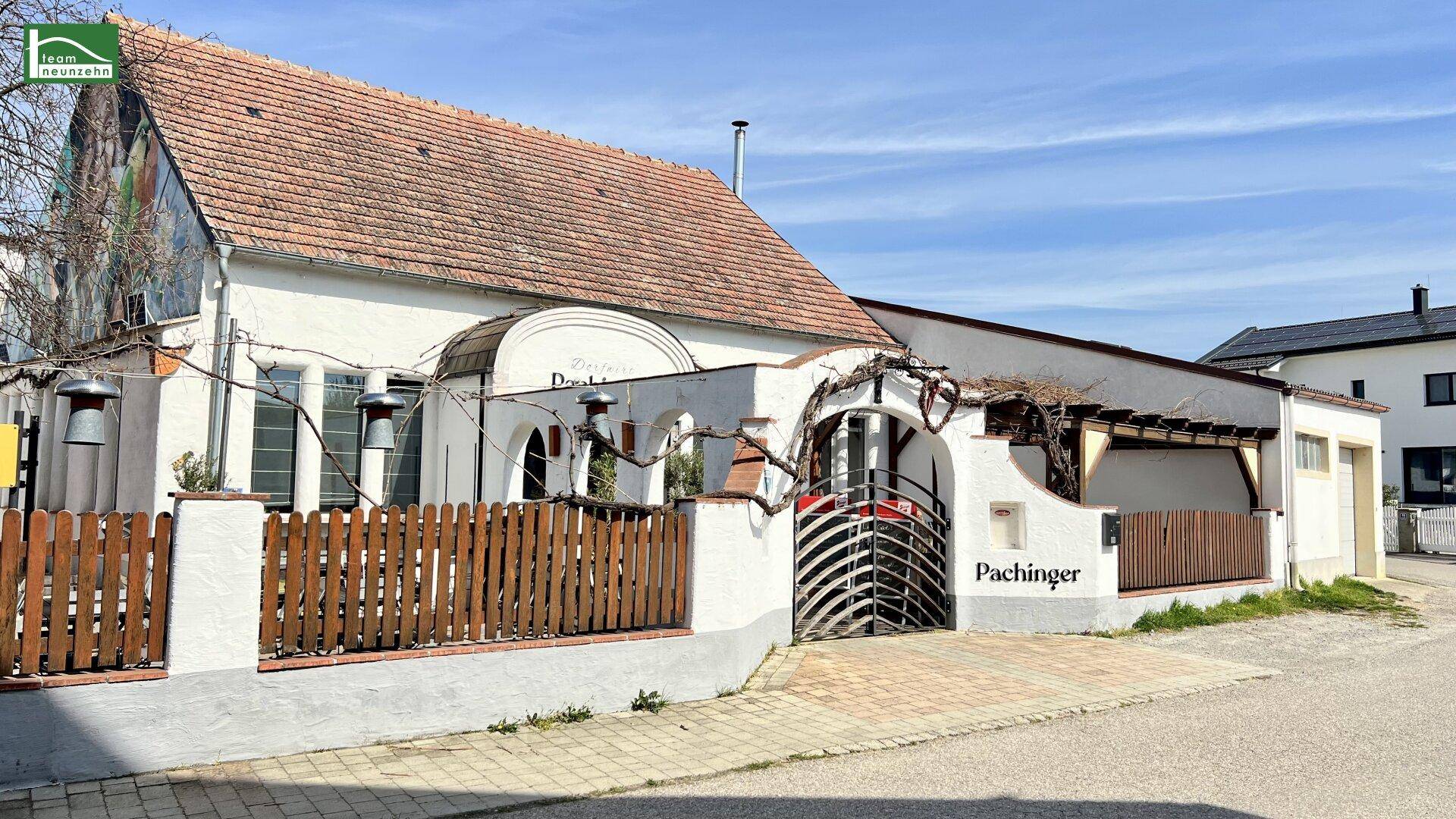 Traditionelles Gebäude mit weißer Fassade, Holzzaun und kunstvollem Eingangstor an der Straße.