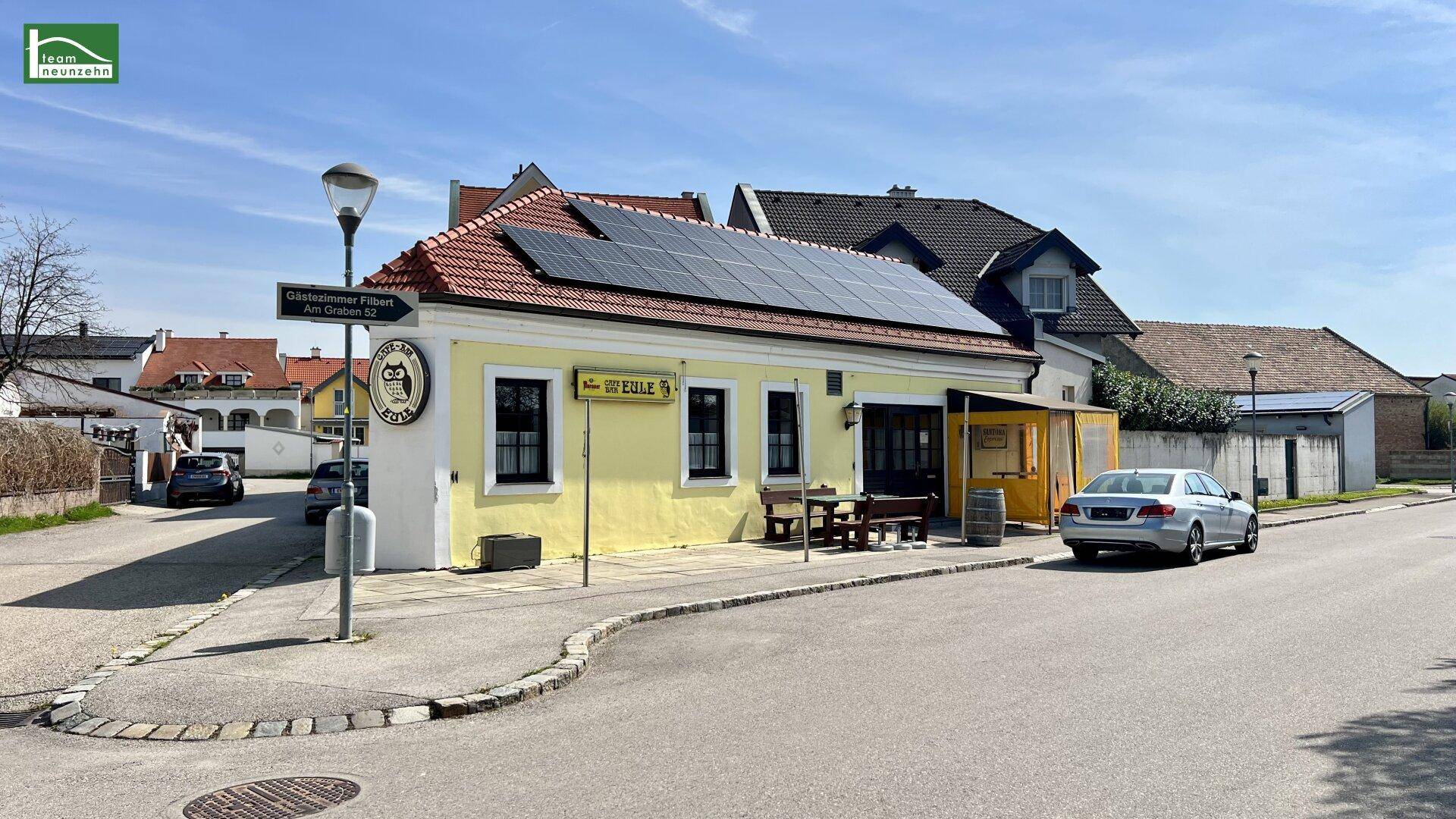 Gebäude an einer Straßenecke mit Photovoltaikanlage auf dem Dach und Außenbereich.