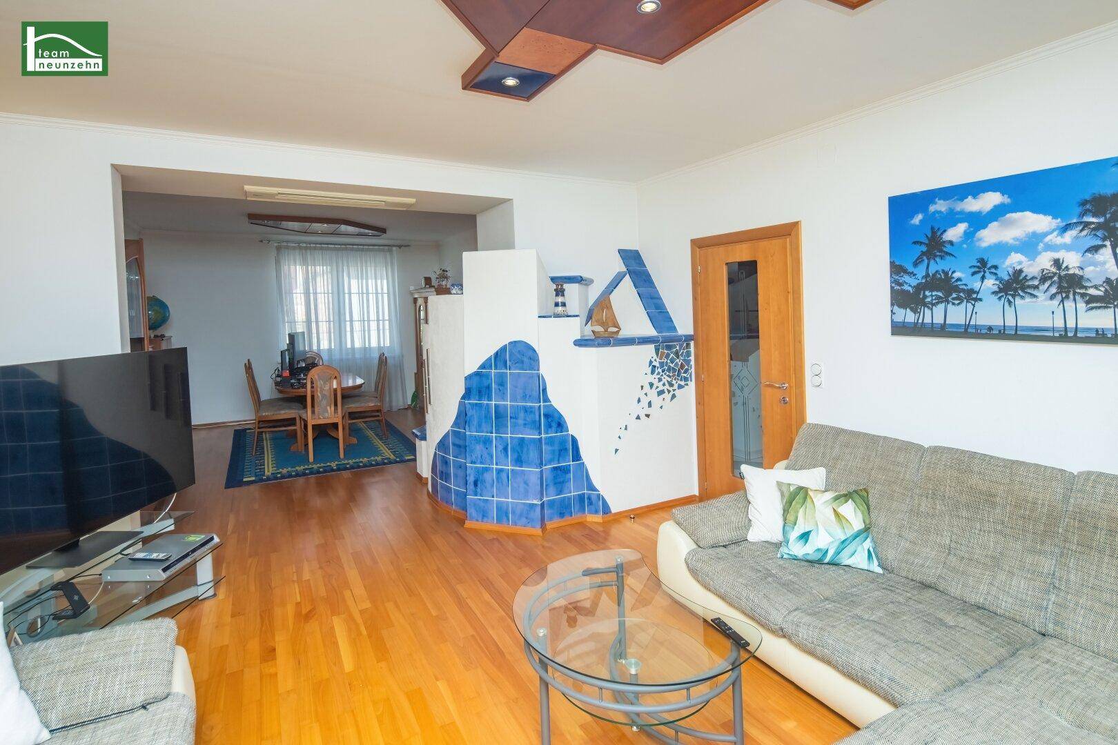 Wohnzimmer mit Holzboden, Sofa, Kachelofen und Blick in den Essbereich.