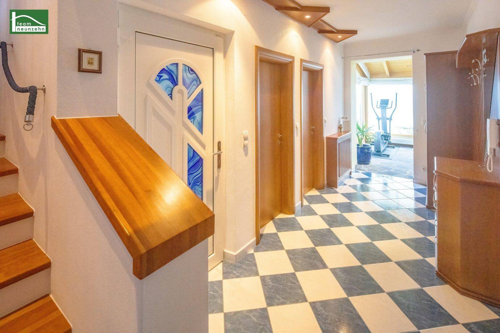 Heller Flur mit Schachbrettmuster-Fliesenboden und Holztreppe.