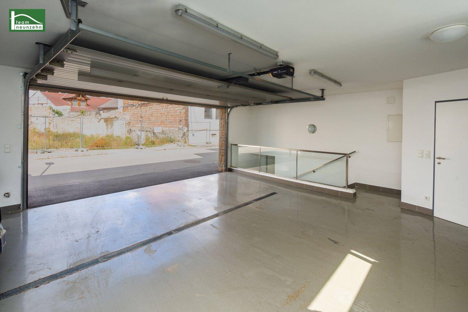 Geräumige Garage mit offenem Tor, Betonboden und Glasgeländer.