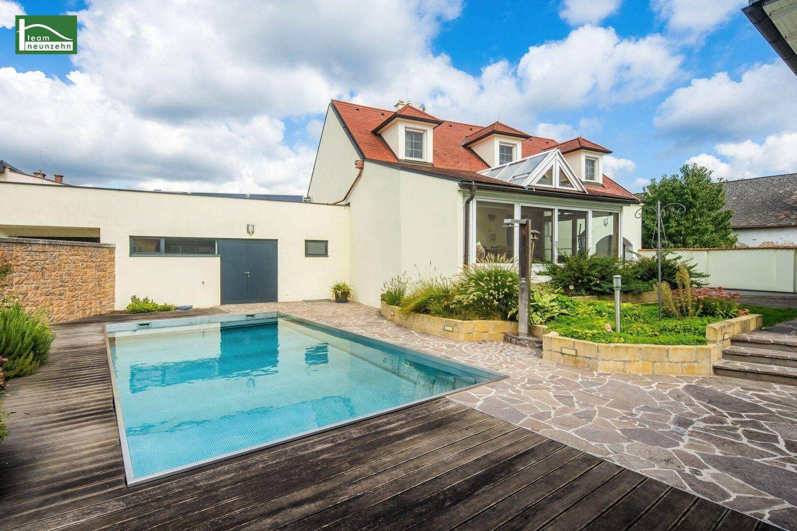 Außenansicht des Hauses mit großem Swimmingpool, Holzdeck und Steinterrasse.