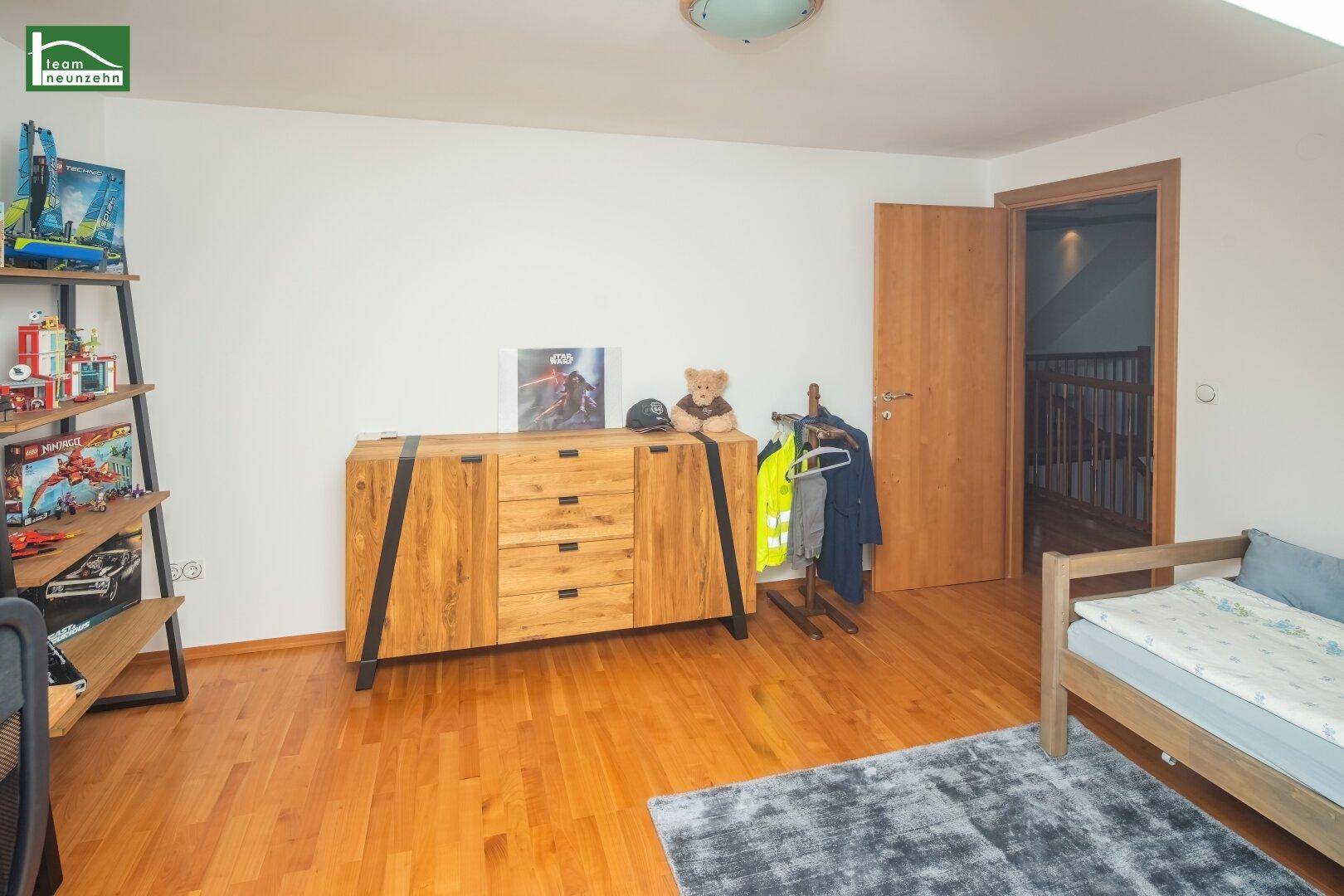 Kinderzimmer mit Holzboden, Holzkommode und modernem Bett.