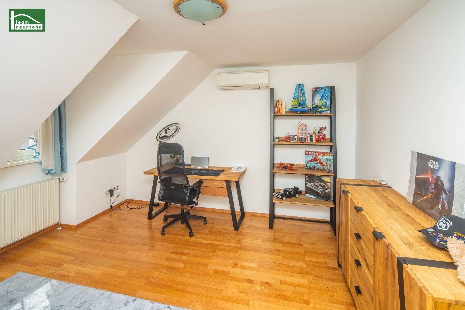 Kinderzimmer mit Holzboden, Schreibtisch, Regal und Klimaanlage.