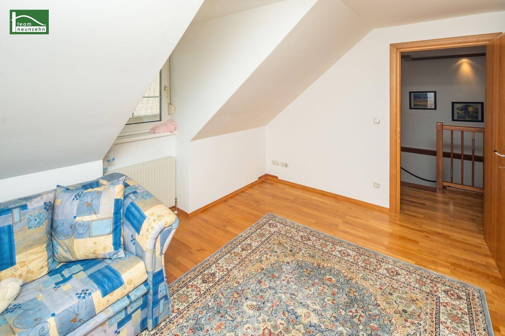 Heller Wohnbereich im Dachgeschoss mit Holzboden, Dachschrägen und farbenfrohem Sofa.