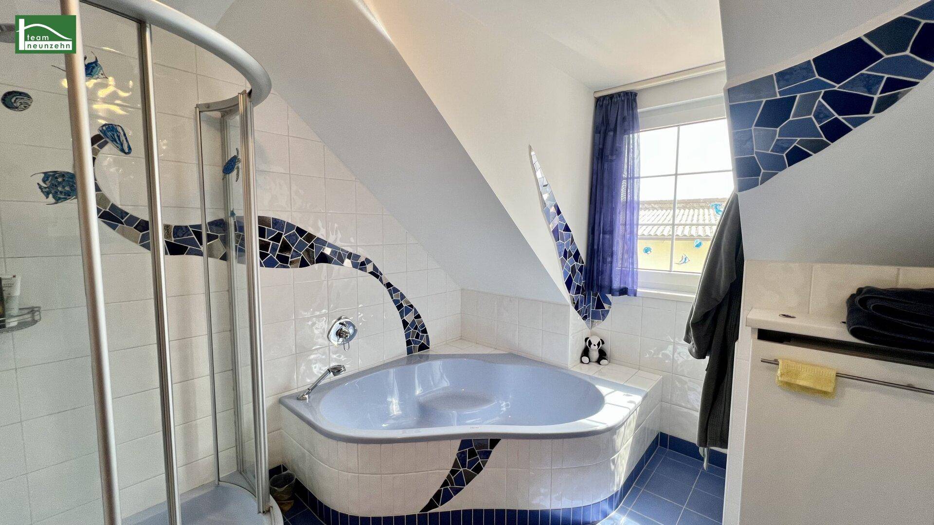 Badezimmer mit Eckbadewanne, Dusche, blauen Fliesen und Fenster im Dachgeschoss.