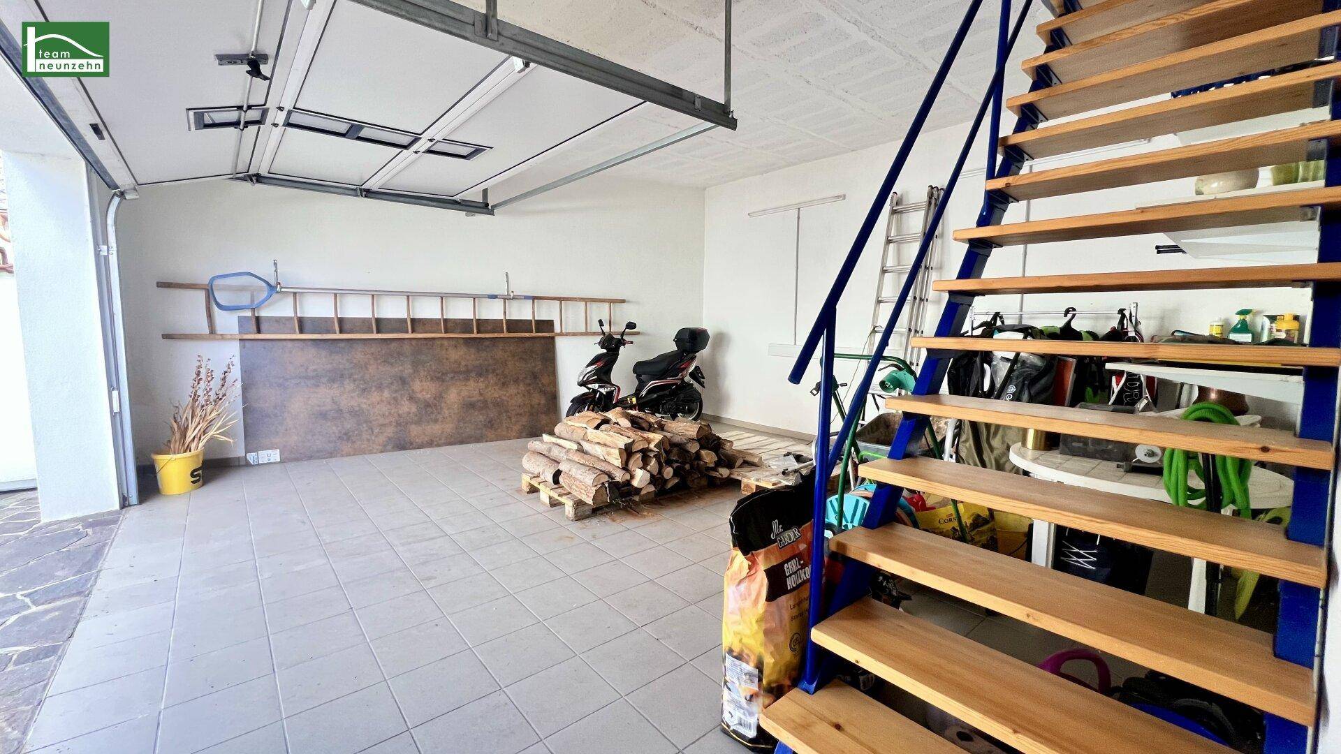 Garage mit Fliesenboden, Holztreppe, Brennholzstapel und Motorrad.
