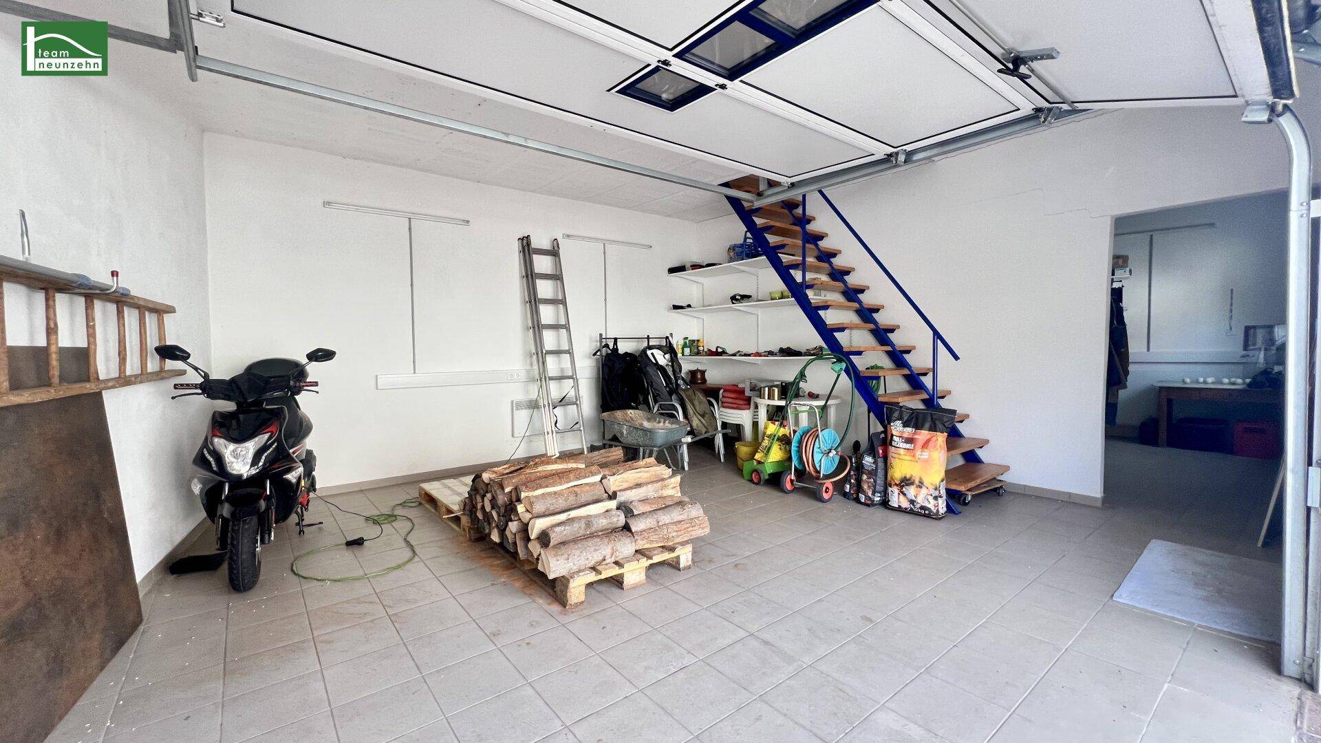 Geräumige Garage mit Fliesenboden, Holztreppe und Brennholzstapel.
