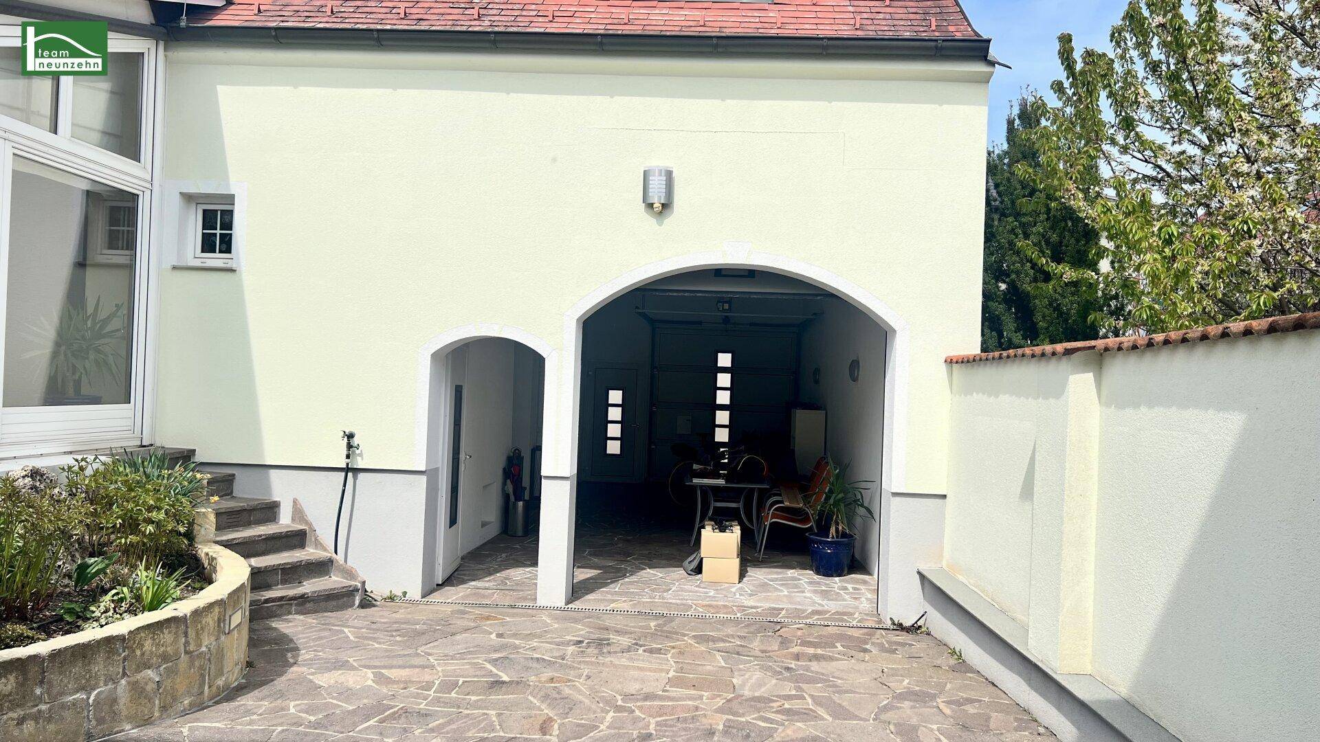 Außenansicht mit gewölbtem Garageneingang und gepflastertem Hofbereich.