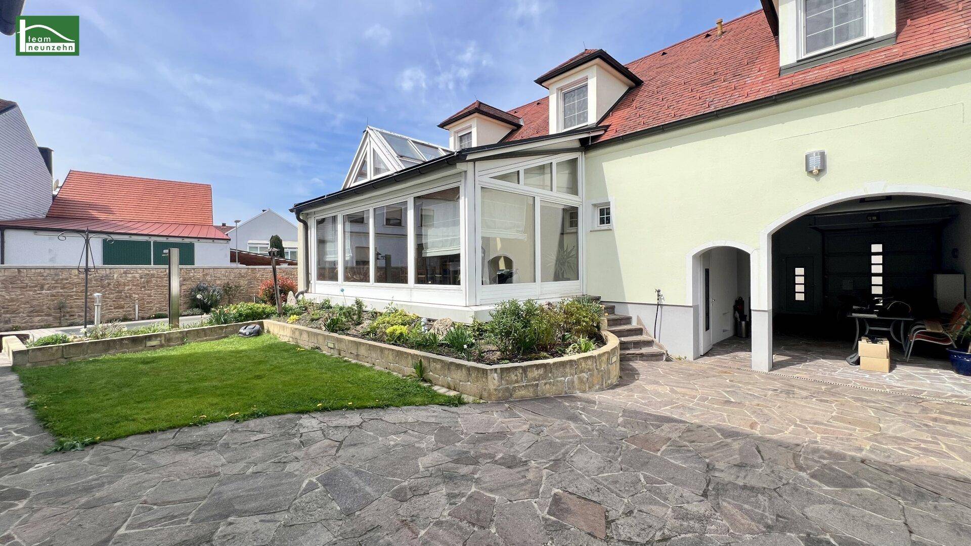 Außenansicht des Hauses mit Wintergarten, gepflastertem Hof und Gartenbereich.