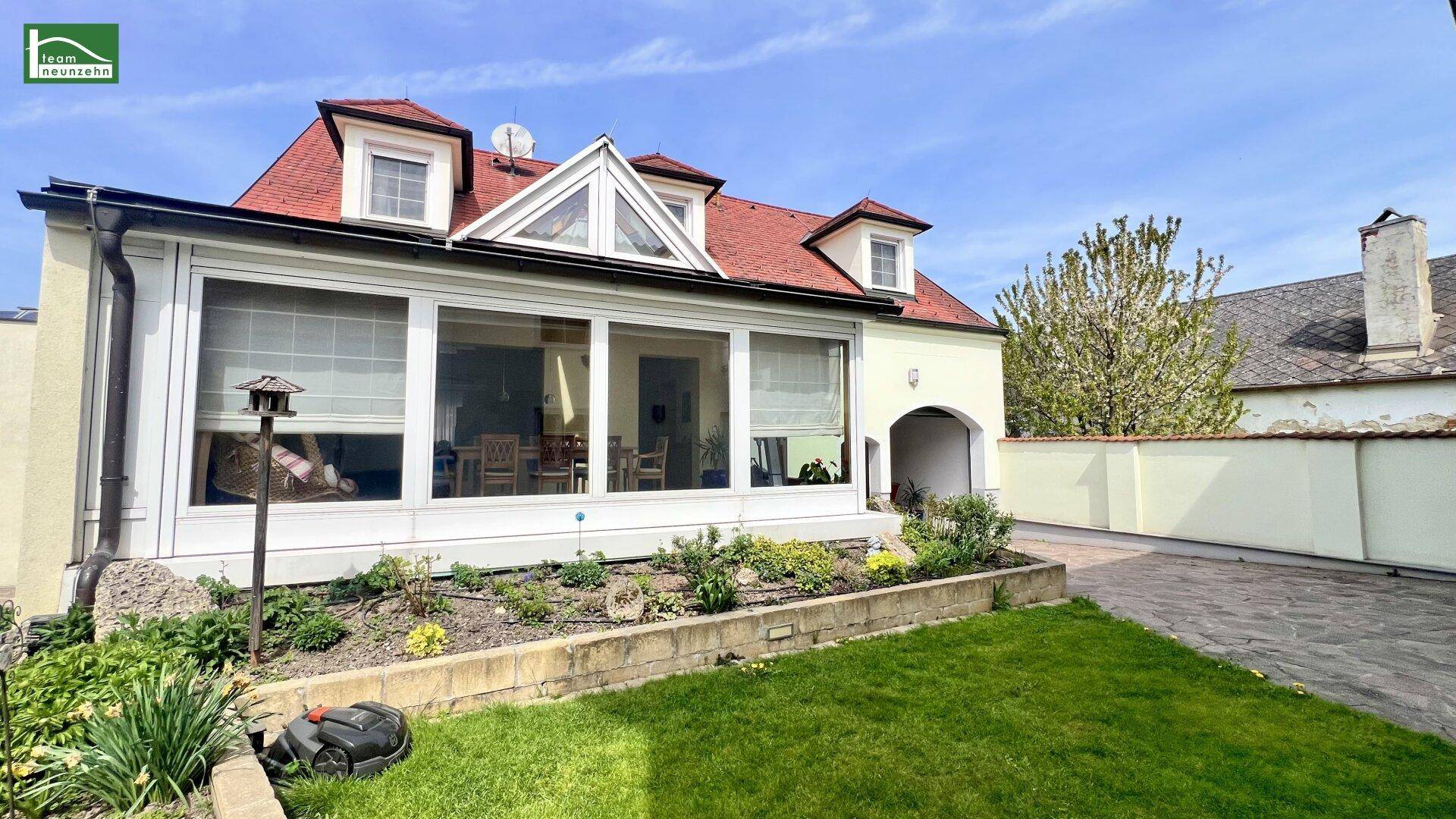 Außenansicht des Hauses mit gepflegtem Rasen, Blumenbeeten und Wintergarten.