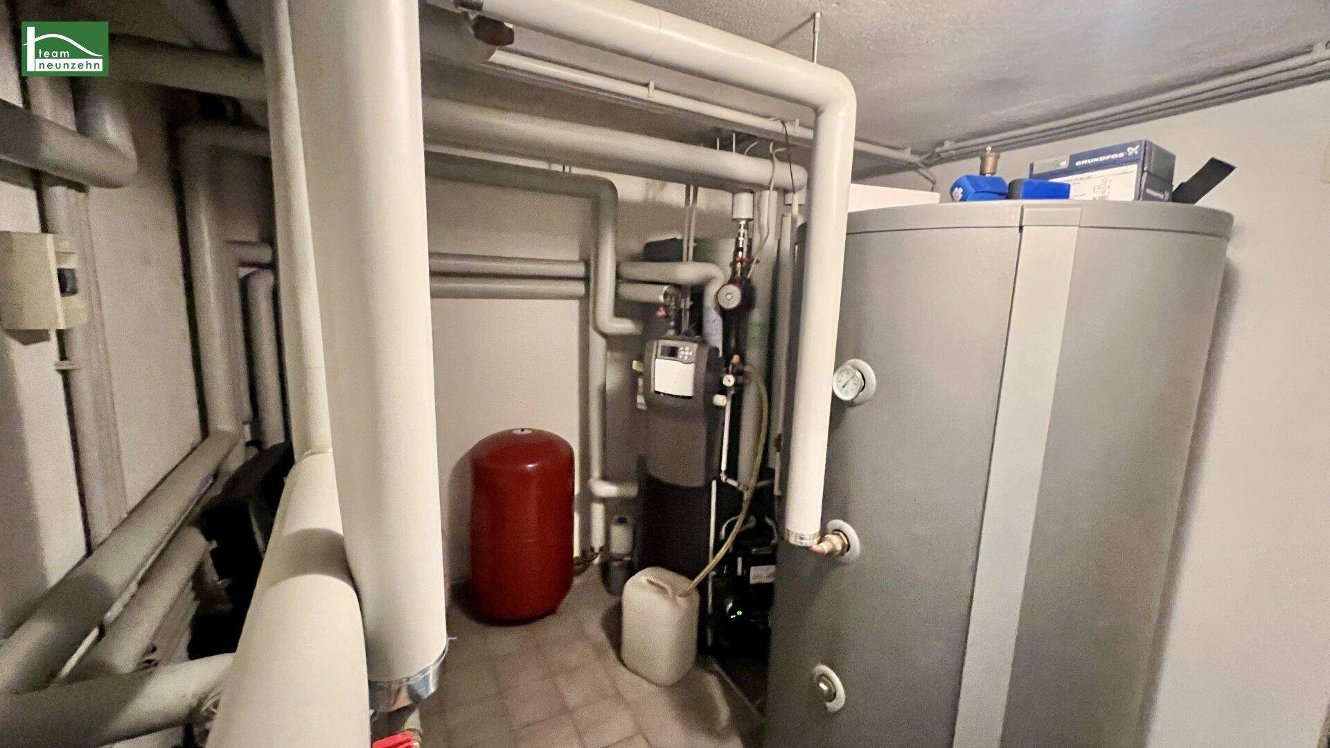 Technikraum im Keller mit Heizungsanlage, Warmwasserspeicher und zahlreichen Rohrleitungen.