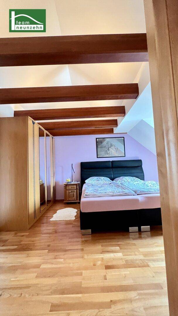 Gemütliches Schlafzimmer im Dachgeschoss mit Holzboden, sichtbaren Balken und Dachschrägen.