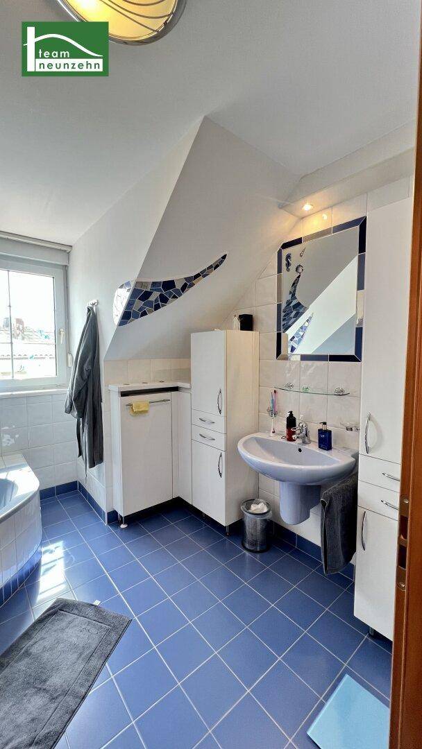 Badezimmer mit Waschbecken, Spiegelschrank, blauen Fliesen und Fenster im Dachgeschoss.