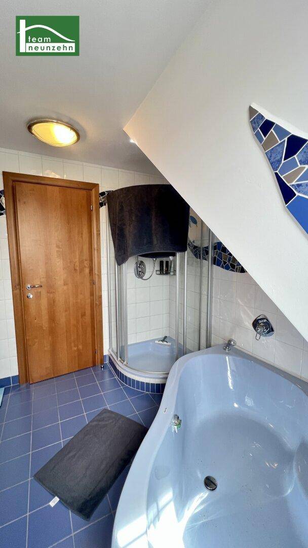 Badezimmer mit Eckbadewanne und Duschkabine, blauen Fliesen und Dachschräge.