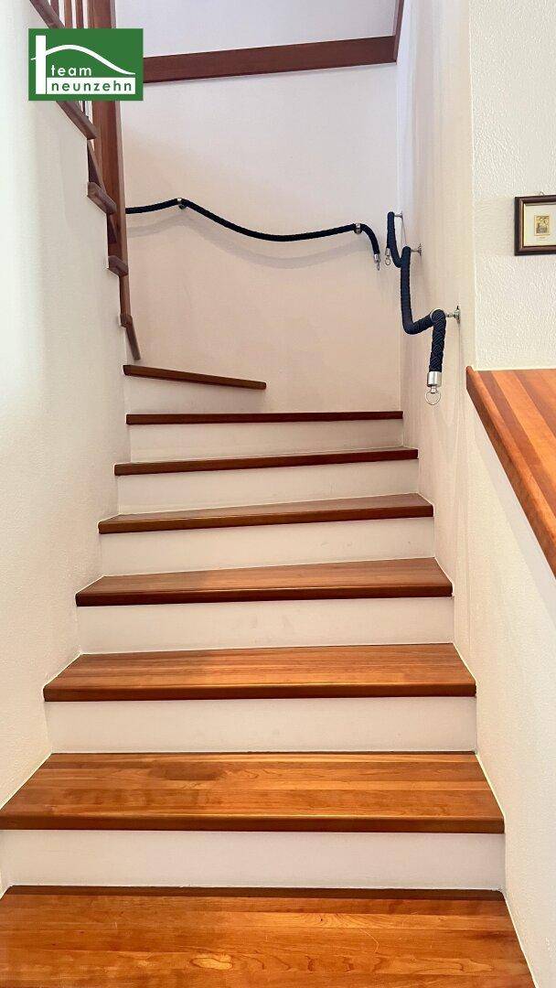 Holztreppe mit Seilgeländer und weiß gestrichenen Wänden.