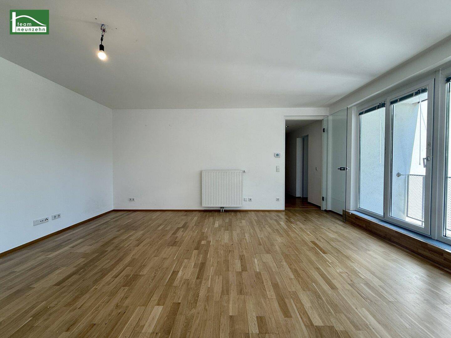 Geräumiger Raum mit Holzboden und großen Fenstern, die viel Licht hereinlassen.
