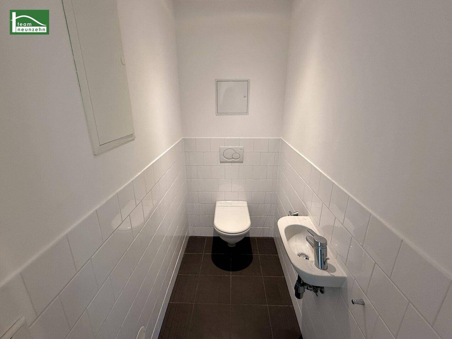 Separates Gäste-WC mit wandhängender Toilette und kleinem Handwaschbecken.