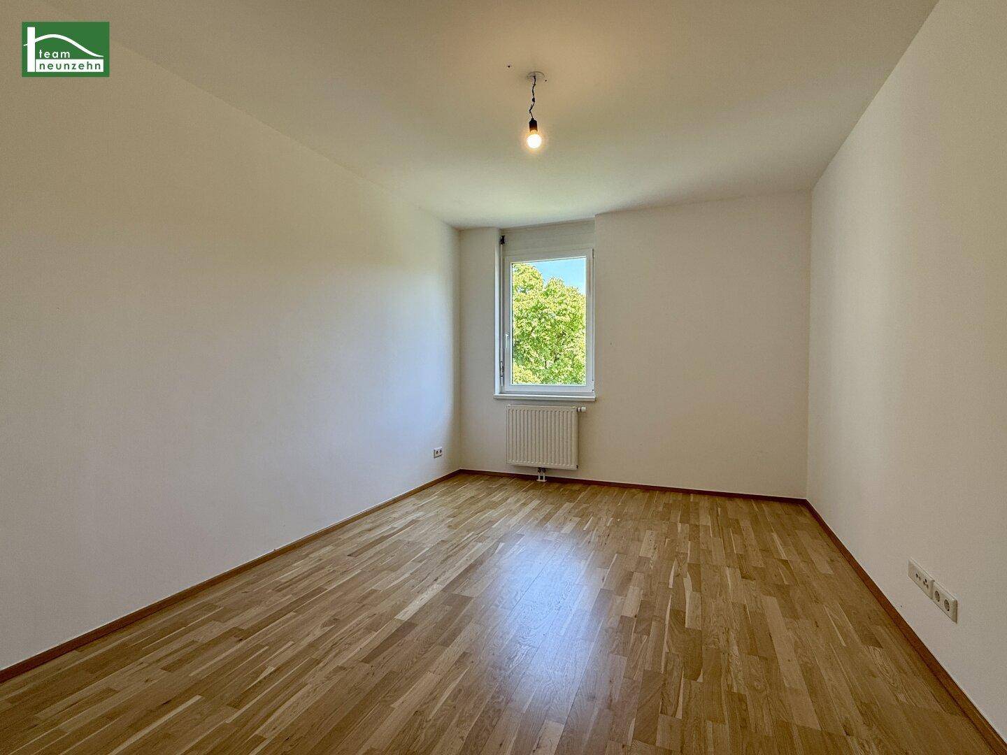 Helles Schlafzimmer mit Holzboden und einem Fenster, das den Blick ins Grüne freigibt.