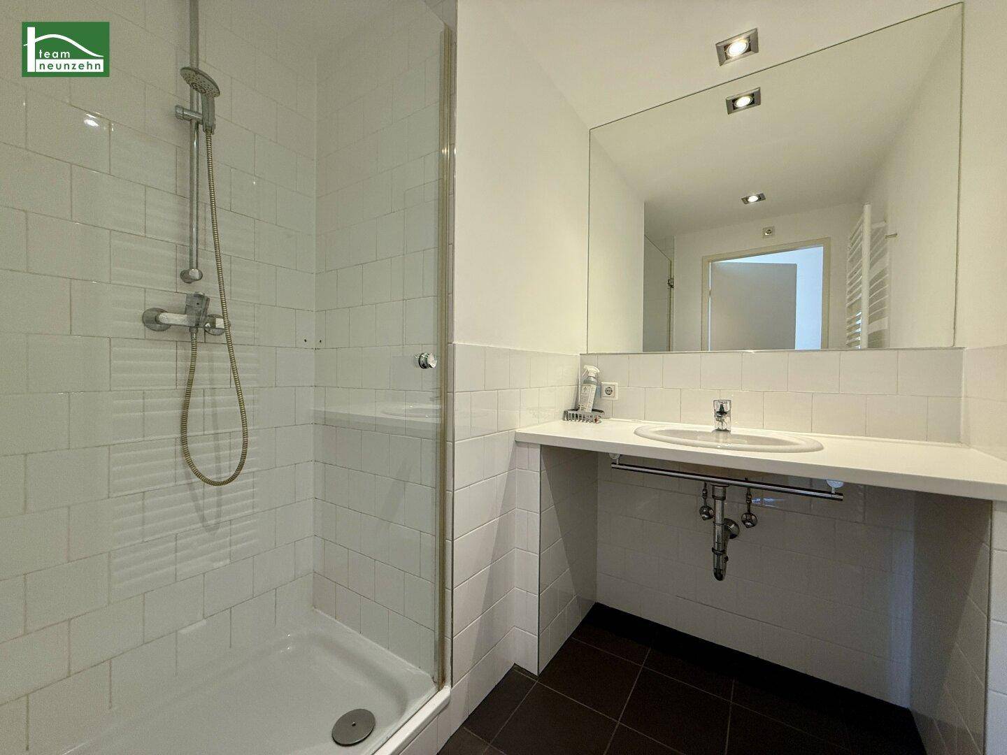 Helles Badezimmer mit Duschkabine, Einzelwaschbecken und weißen Wandfliesen.