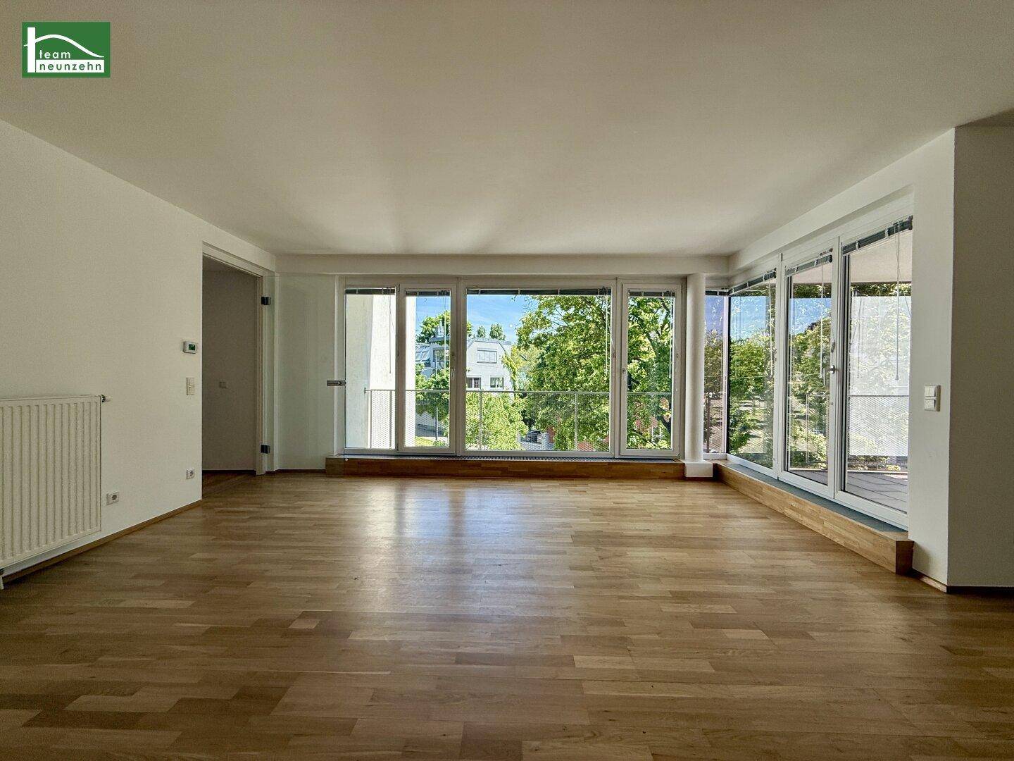 Geräumiges Wohnzimmer mit großen Fenstern, die viel Tageslicht hereinlassen und Holzboden.