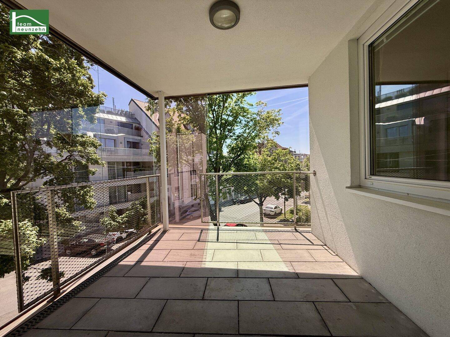 Heller Balkon mit Fliesenboden und Glasbrüstung, bietet einen Blick auf die Umgebung.