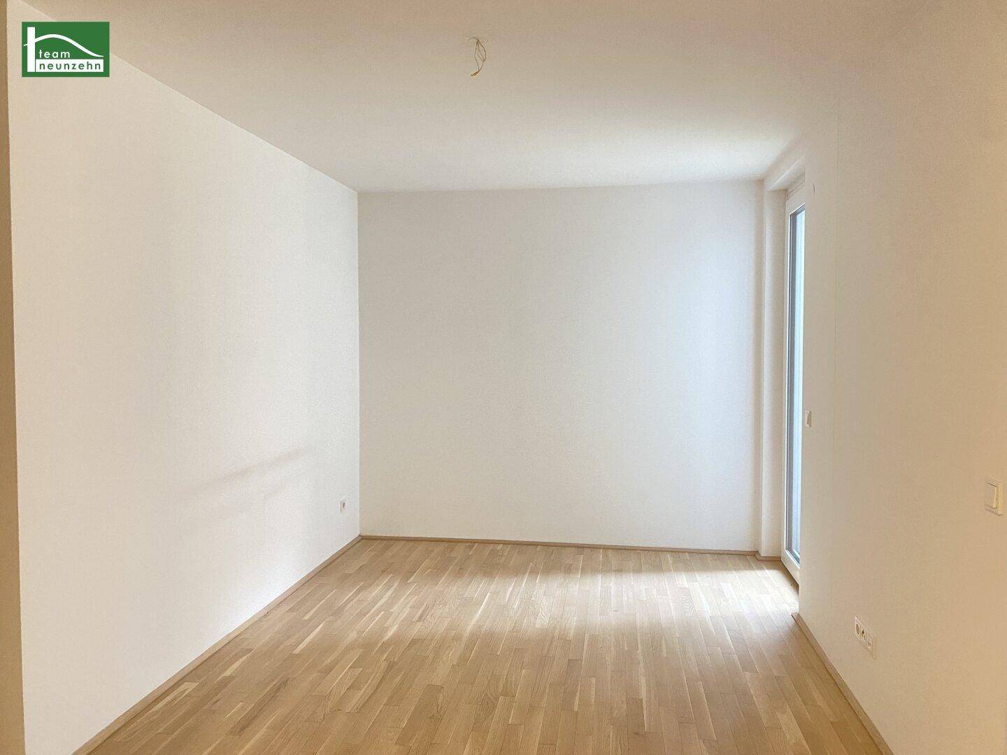 Leerer Raum mit Parkettboden und großen Fenstern, die viel Tageslicht hereinlassen.