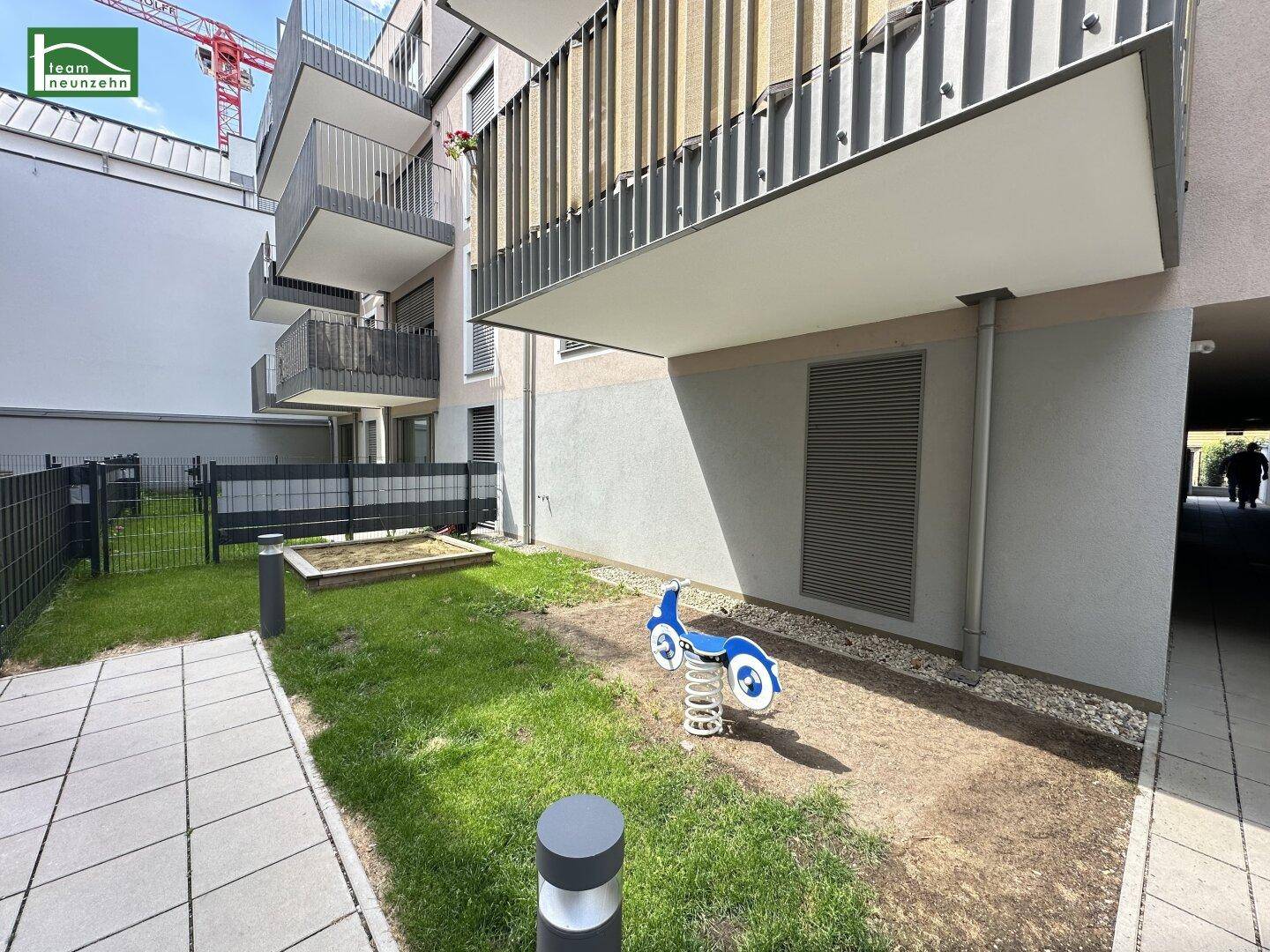 Außenbereich eines modernen Wohngebäudes mit kleinem Spielplatz, Sandkasten und Balkonen.