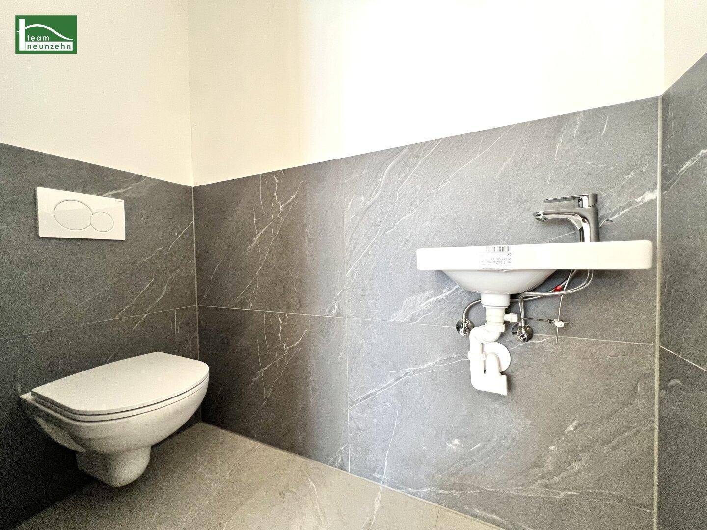 Modernes Gäste-WC mit grauen Fliesen, wandhängendem WC und kleinem Waschbecken.