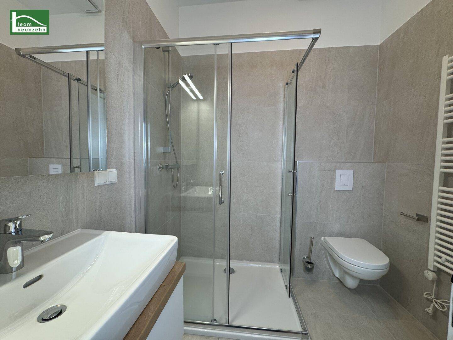 Modernes Badezimmer mit Duschkabine, Waschbecken und wandhängendem WC in hellen Grautönen.