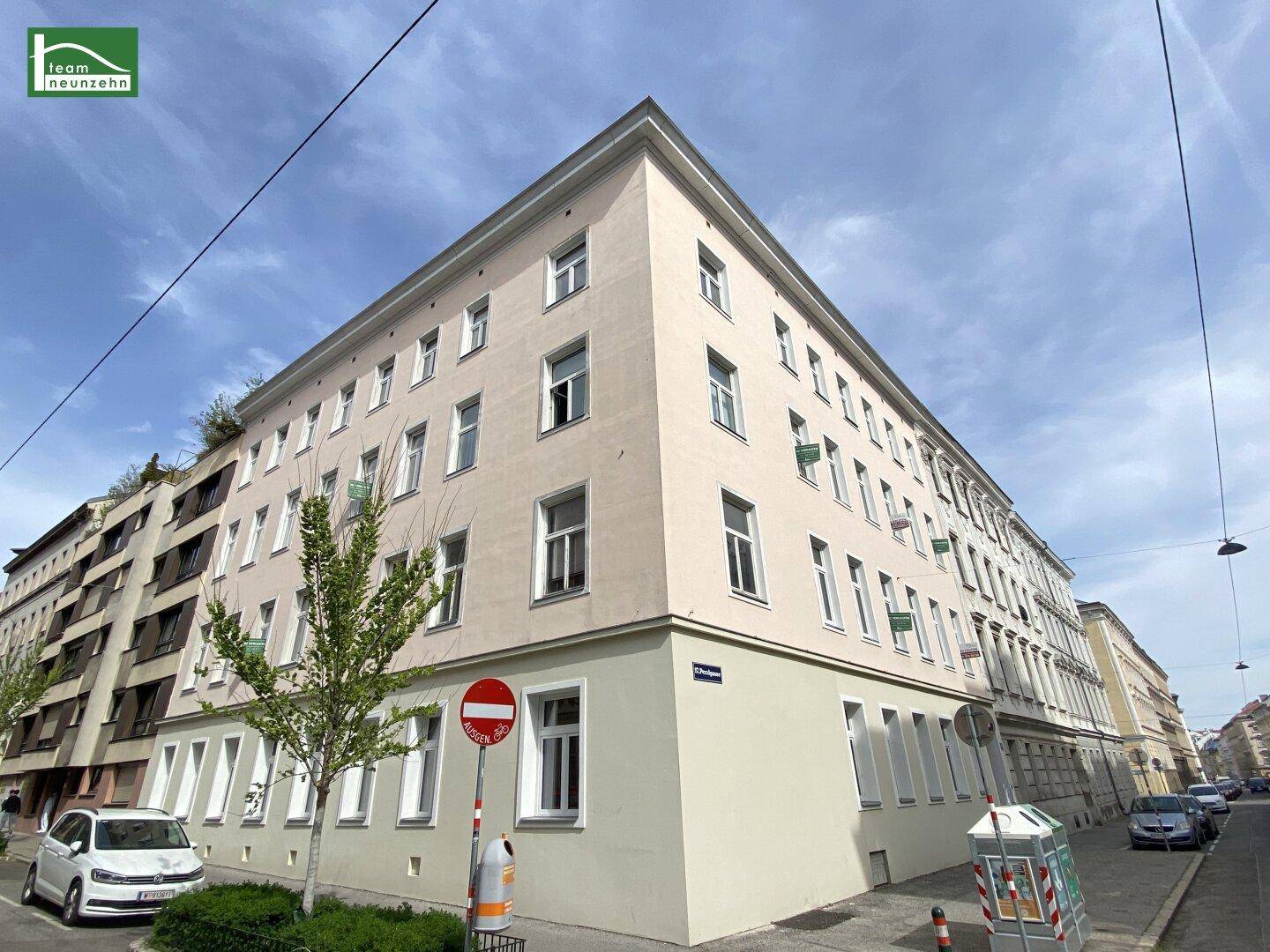 Eckgebäude in einer städtischen Umgebung mit mehreren Stockwerken und vielen Fenstern.