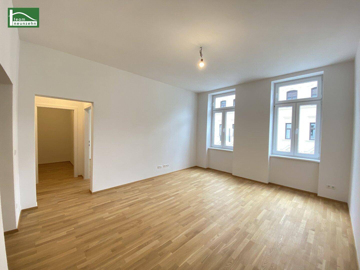 Helles, leeres Zimmer mit Parkettboden und zwei großen Fenstern, bereit zur individuellen Gestaltung.
