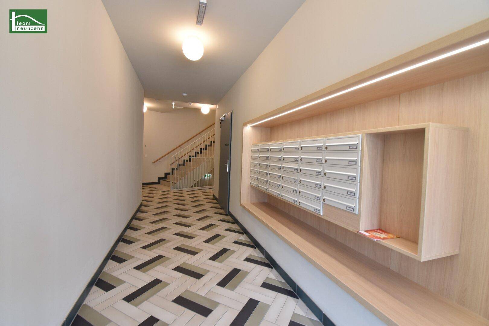 Moderner Eingangsbereich eines Mehrfamilienhauses mit gemustertem Fliesenboden und integrierter Briefkastenanlage.