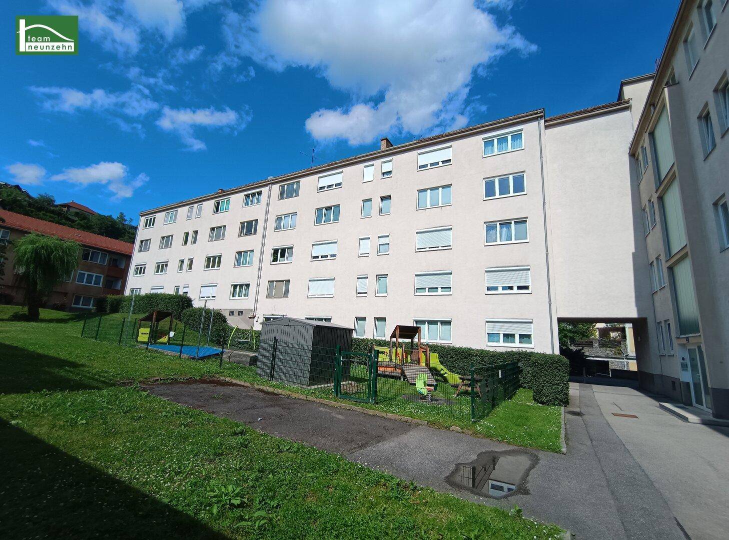 Mehrfamilienhaus mit gepflegter Grünanlage und Kinderspielplatz im Freien.