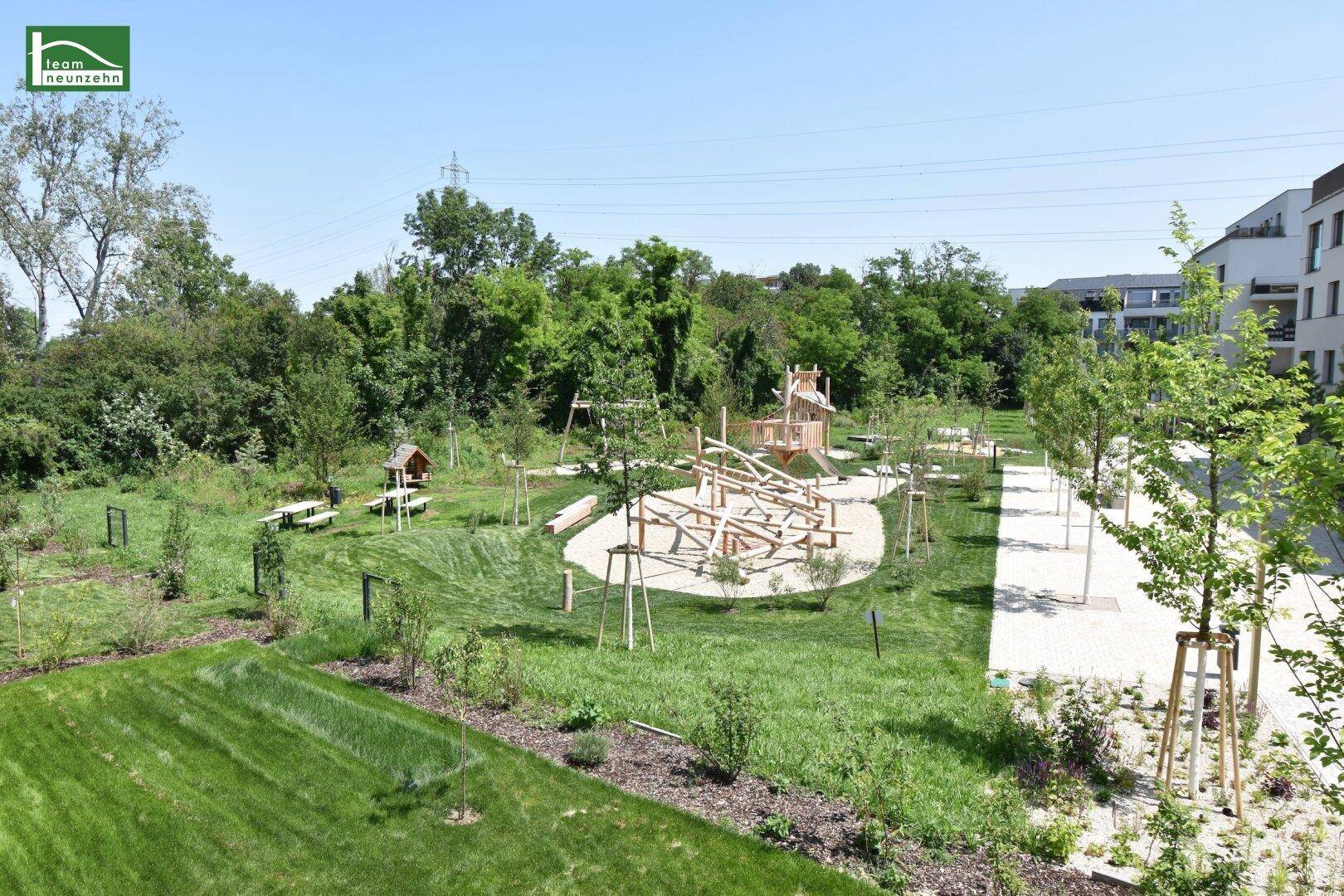 Weitläufiger Spielplatz mit Holzspielgeräten und viel Grünfläche in einer modernen Wohnanlage.