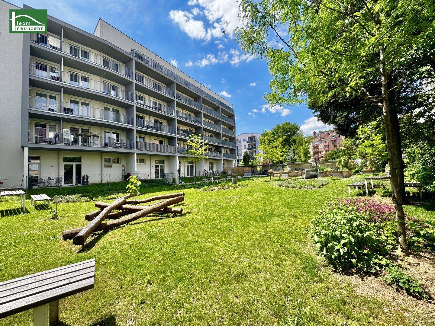 Weitläufiger Gemeinschaftsgarten mit Rasenfläche und natürlichen Holzspielelementen vor dem Wohngebäude.