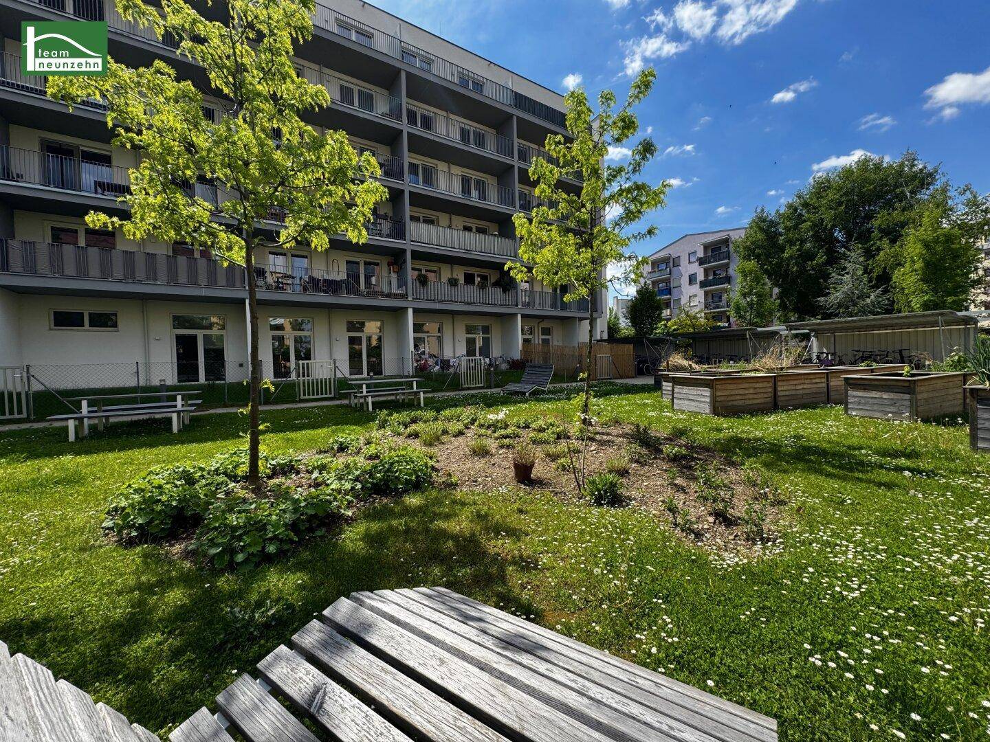 Gepflegter Gemeinschaftsgarten mit Sitzbänken und blühenden Pflanzen vor der modernen Wohnanlage.
