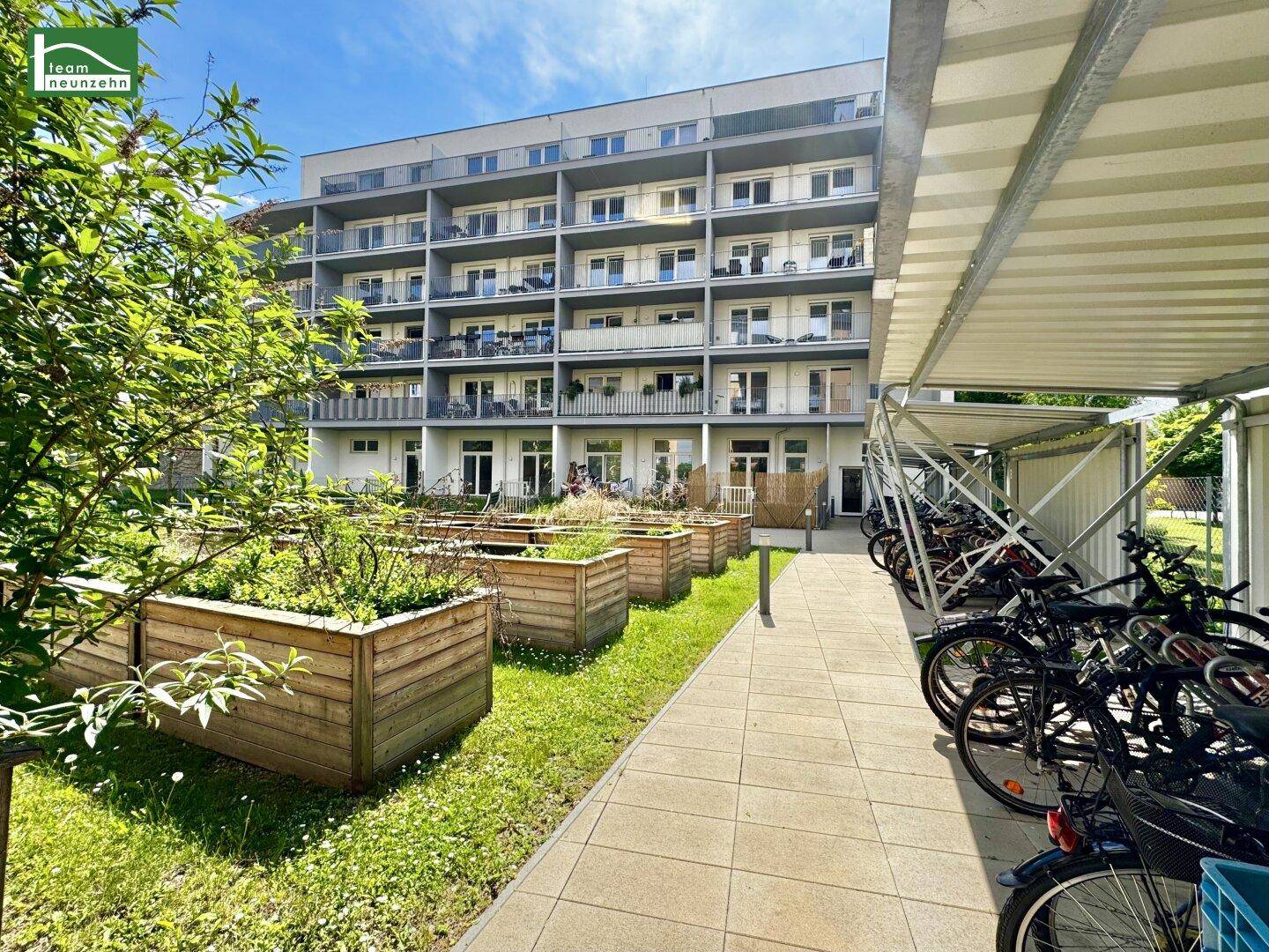 Modernes Apartmentgebäude mit Balkonen, begrüntem Außenbereich und überdachtem Fahrradabstellplatz.