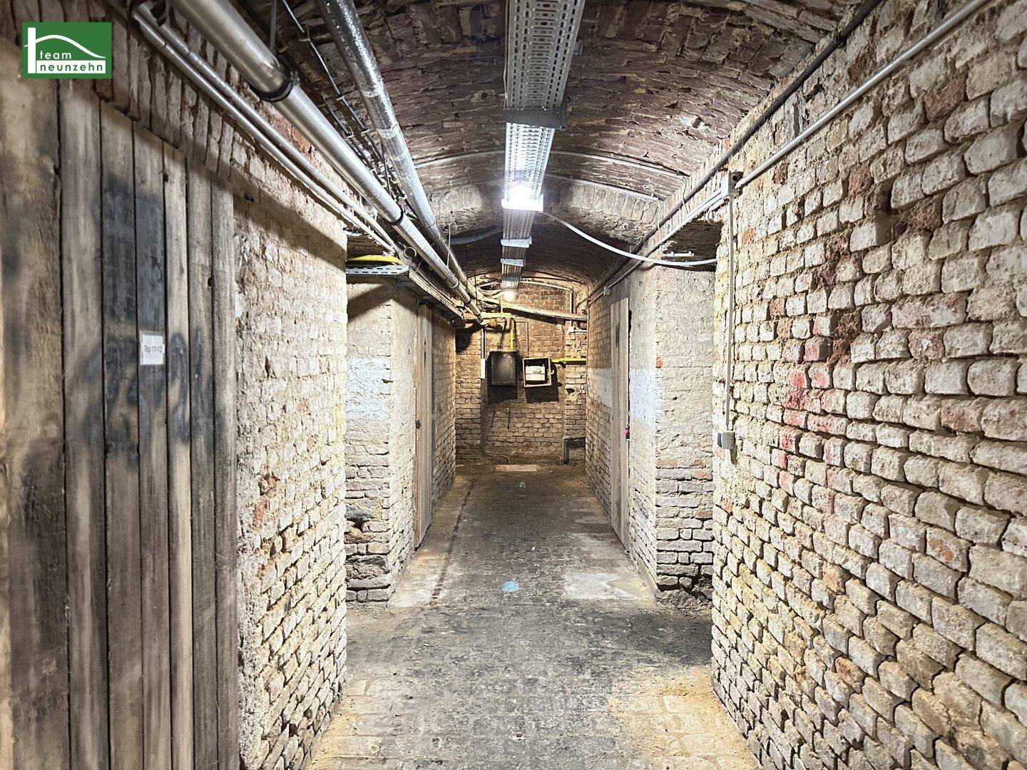 Historischer Kellergang mit unverputzten Ziegelwänden und sichtbaren Leitungen an der Decke.