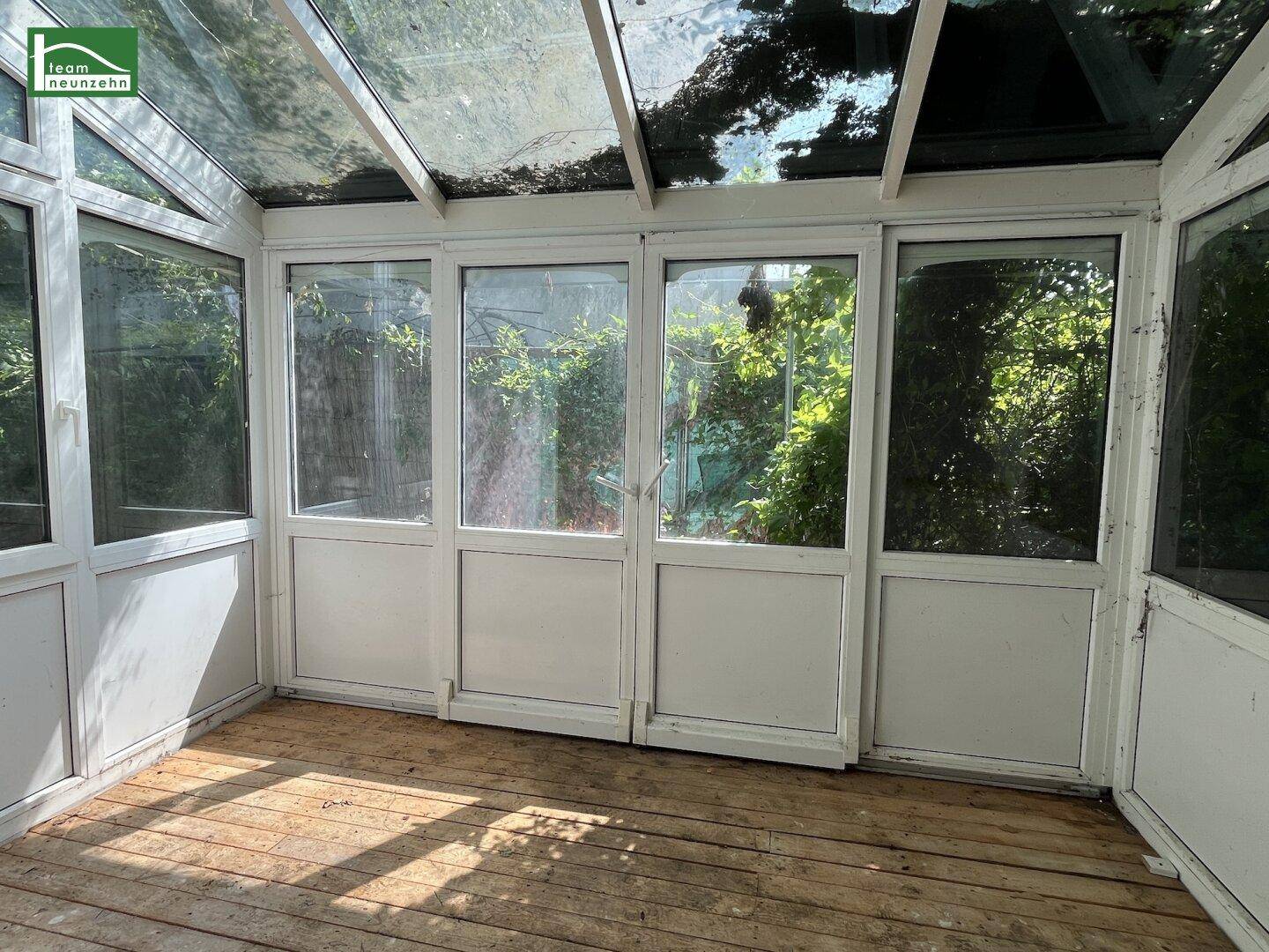 Heller Wintergarten mit Glasdach und Blick ins Grüne, ausgestattet mit Holzfußboden.
