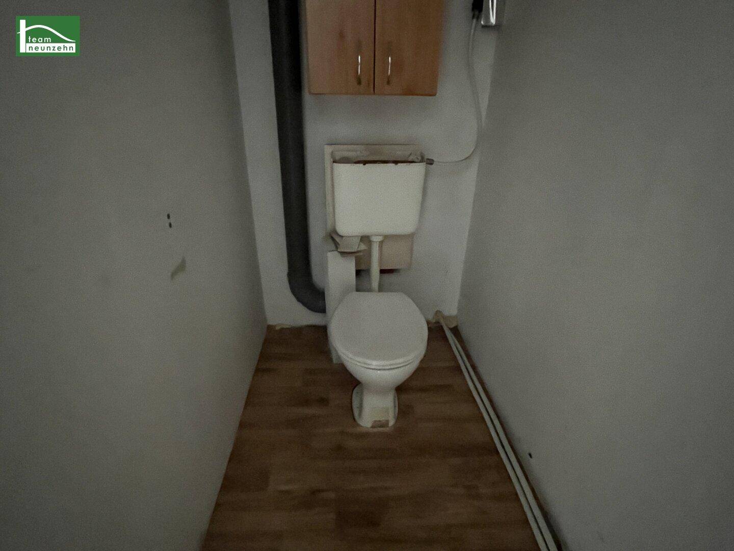 Kleines Gäste-WC mit einfacher Toilette und Holzoptik-Laminatboden.