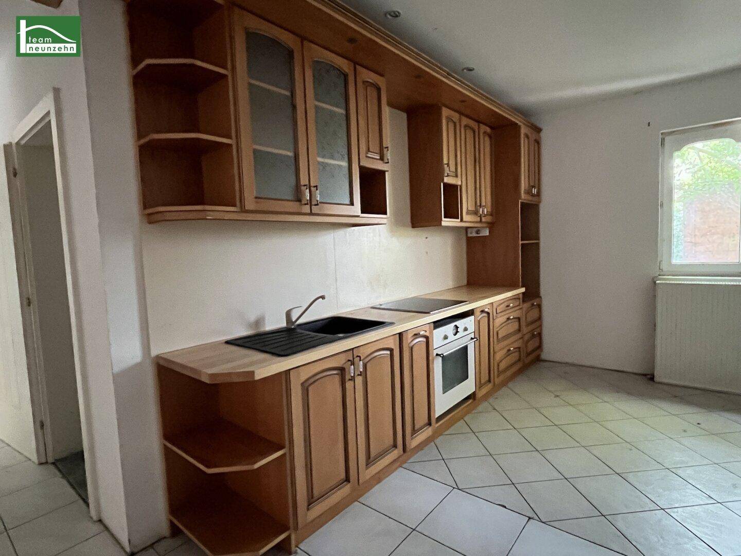 Traditionelle Einbauküche mit Holzschränken, Spüle und Kochfeld, gefliestem Boden und Fenster.
